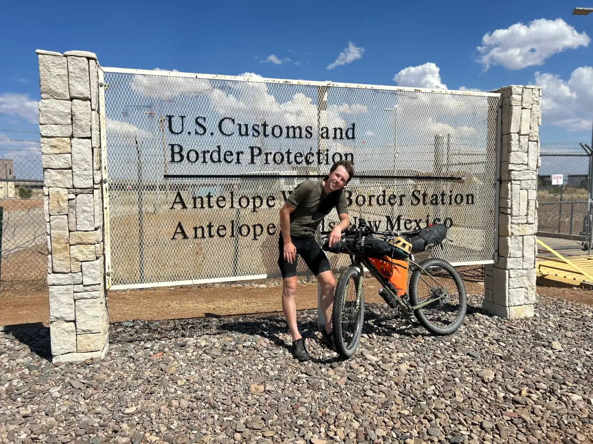 Brad completes tour divide, standing next to U.S. border customs sign near Mexico border